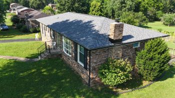 Aerial view of brick home with a newly replaced shingle roof and chimney on a grassy lot